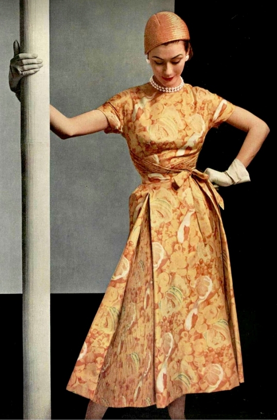 Anne Gunning in silk print dress of various shades of yellow with pleated panels in the skirt and a crossed bodice by Givenchy, photo by Pottier, 1953